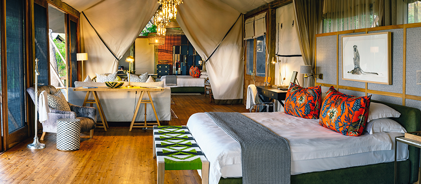 Spacious luxury tent interior at Tuludi Camp featuring a king-size bed with vibrant cushions, elegant furnishings, and a private plunge pool, surrounded by natural light and safari-inspired decor.