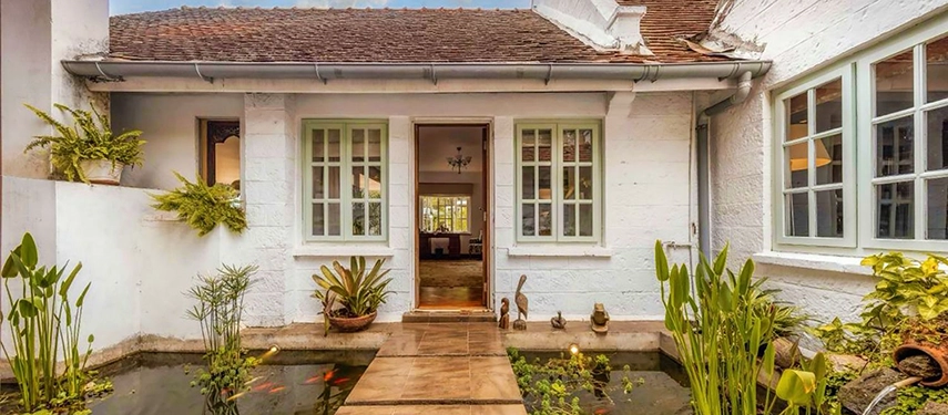 The inner courtyard entrance of Hamilton House, with a stepping-stone path crossing a small ornamental fish pond set between whitewashed walls, potted tropical plants and carved wooden sculptures