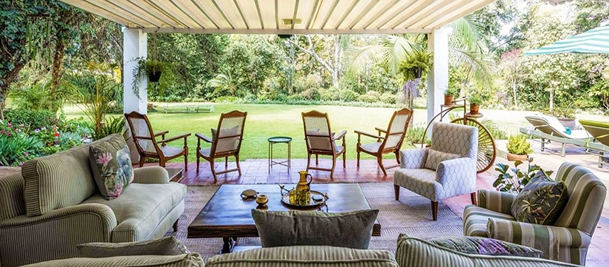 The expansive covered veranda at Hamilton House, furnished with sofas, cane chairs and armchairs beneath a striped awning and looking out over wide, manicured garden lawns