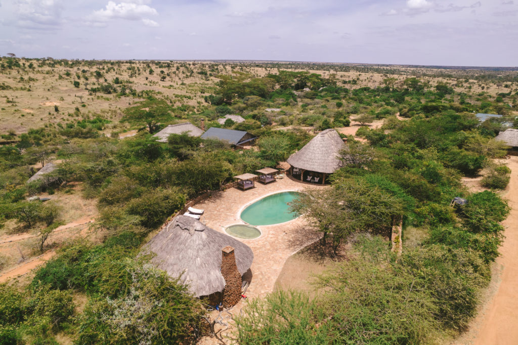 Aerial view of El Karama Lodge's thatched cottages and stone-paved pool set among acacia bush on the Laikipia plains, Kenya.