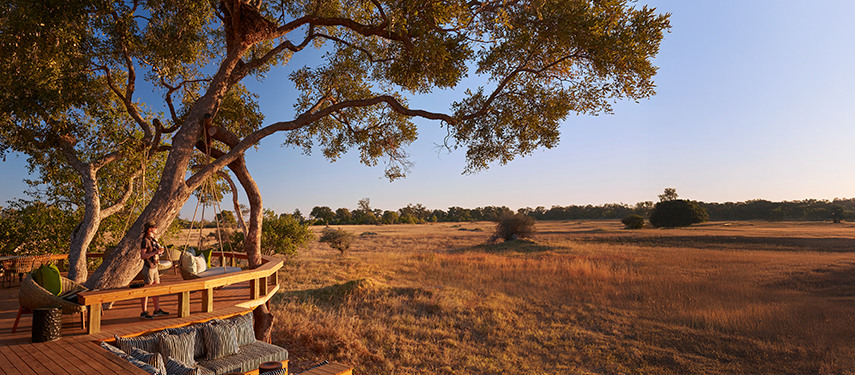 Deck overlooking the expansive plains of Botswana, featuring a person relaxing in a luxurious setting surrounded by nature, highlighting the refined safari experience at Tuludi Camp.