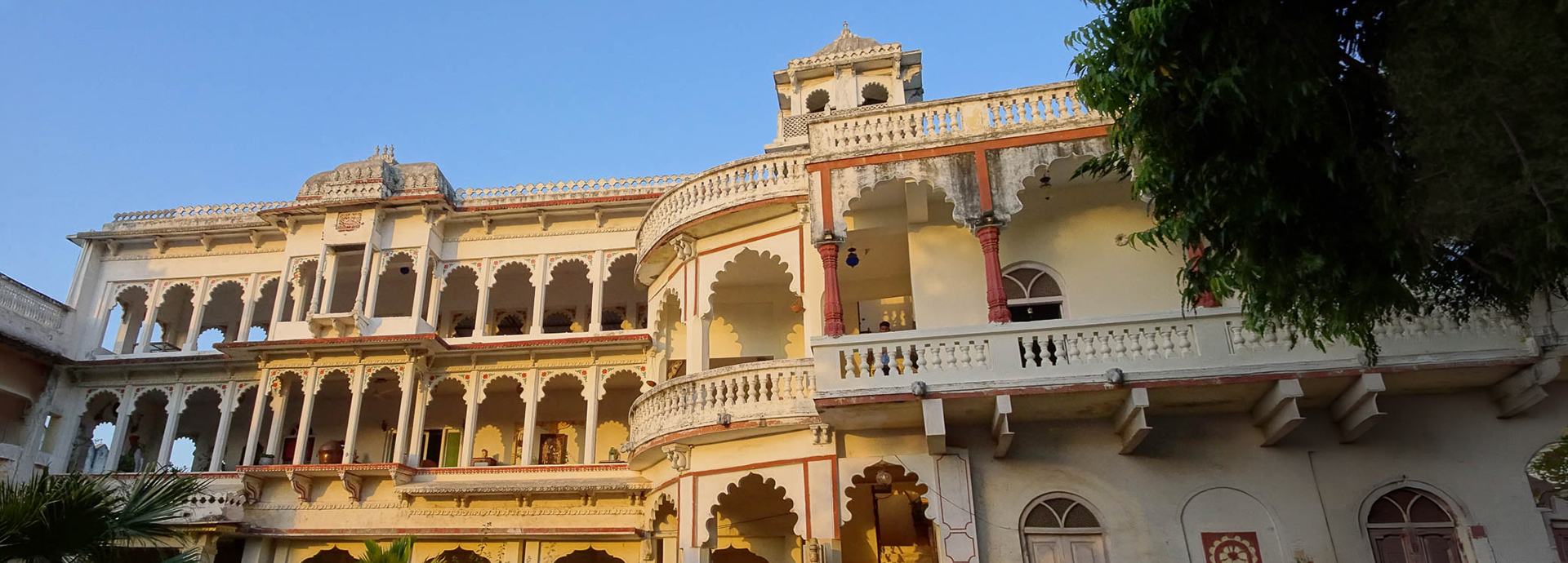 Golden hour light on the arched facade of Darbargadh Poshina, its carved balconies and domed turret rising against a clear blue sky