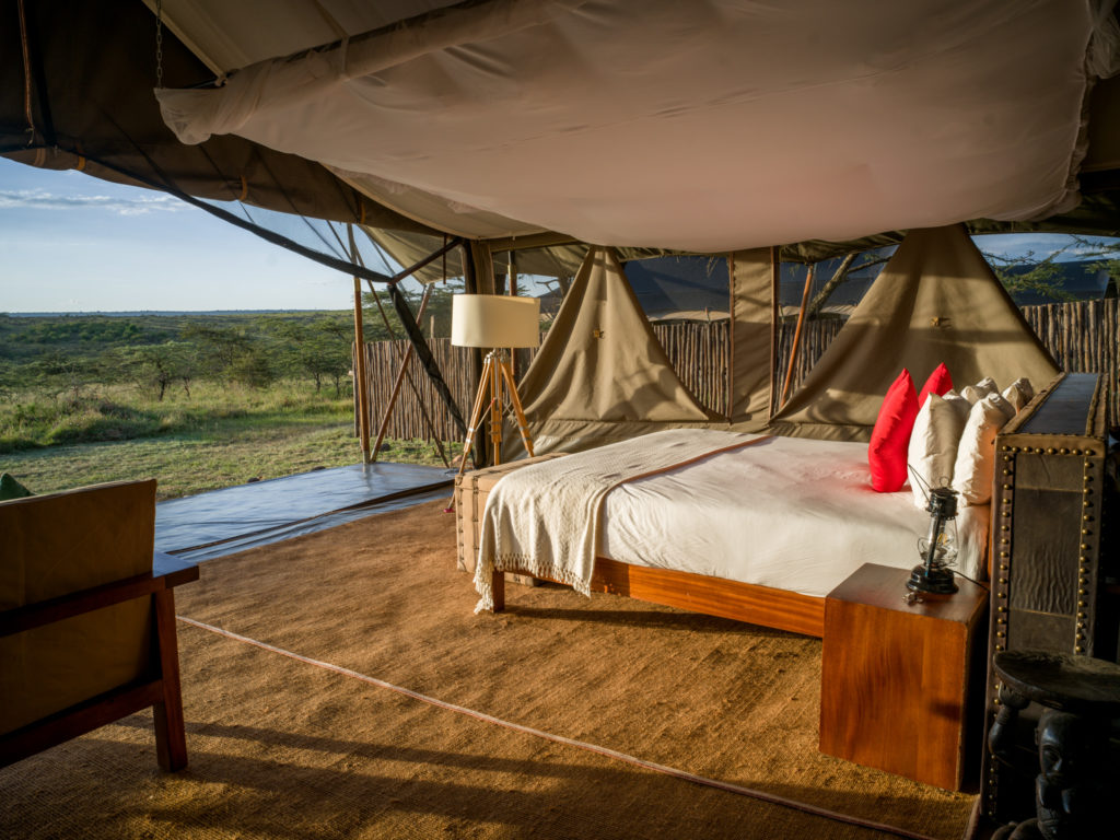 Superior double tent at Kandili Camp in golden light, with a mosquito net, tripod floor lamp and hurricane lantern beside the bed.