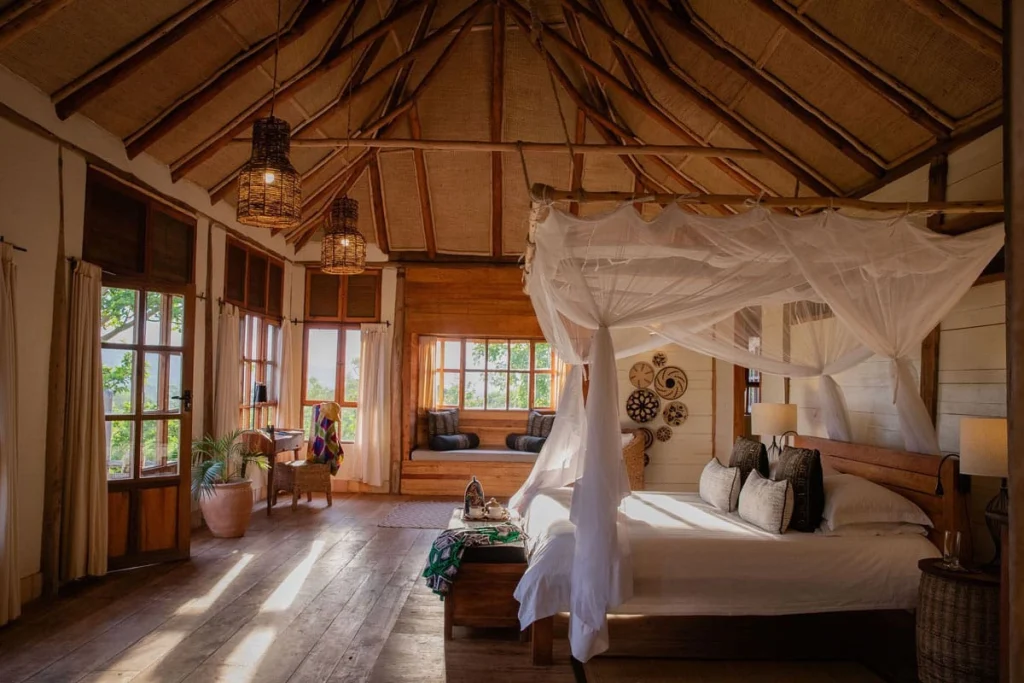 Light-filled bedroom at Kyambura Gorge Lodge, Uganda, with four-poster bed, mosquito net and thatched ceiling