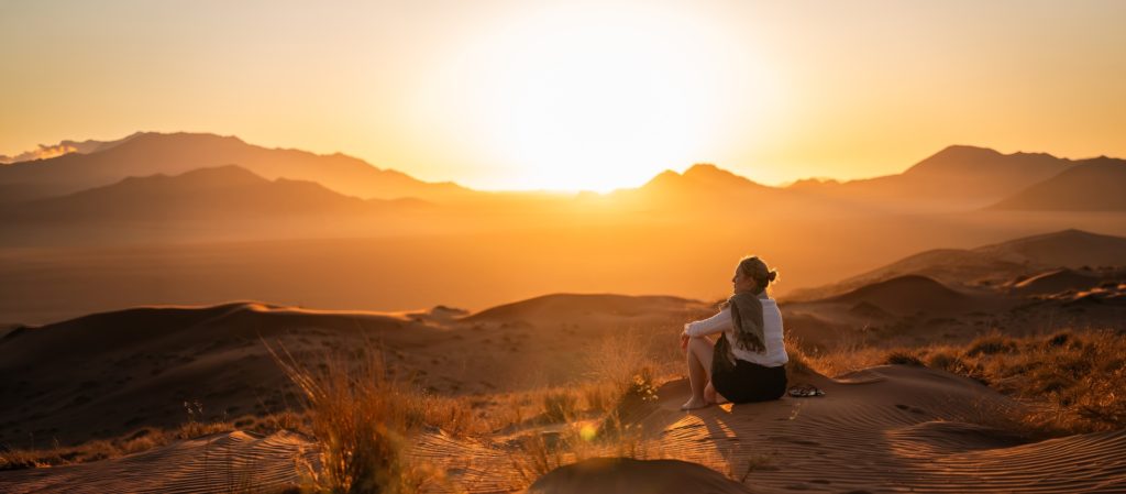 Woman sitting on the dunes of Namibia at Wolwedans Dune Camp at sunset.