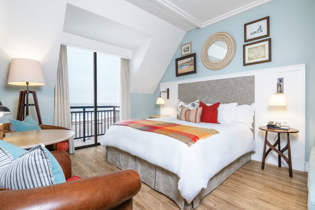 Standard Room at Strand Hotel Swakopmund with a private balcony overlooking the Atlantic Ocean and a plaid throw folded across the bed