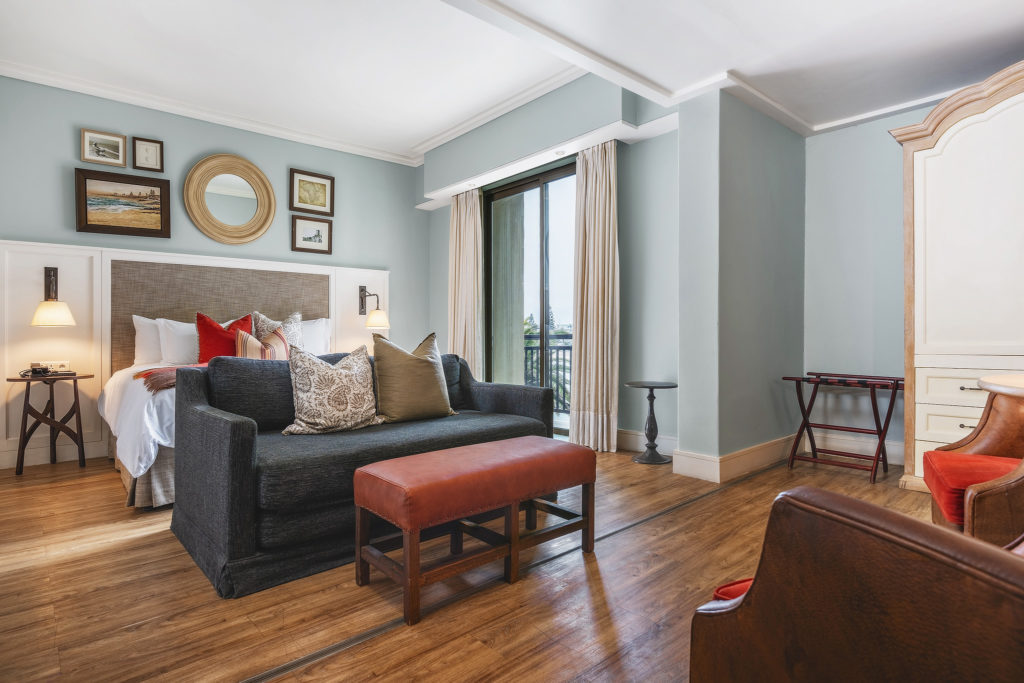 Standard Family Room at Strand Hotel Swakopmund with a sofa bed, armchair and glimpses of the ocean through the balcony doors