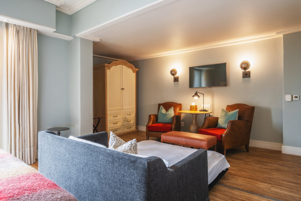 Seating nook in a Standard Family Room at Strand Hotel Swakopmund with leather armchairs, wall-mounted television and built-in wardrobe
