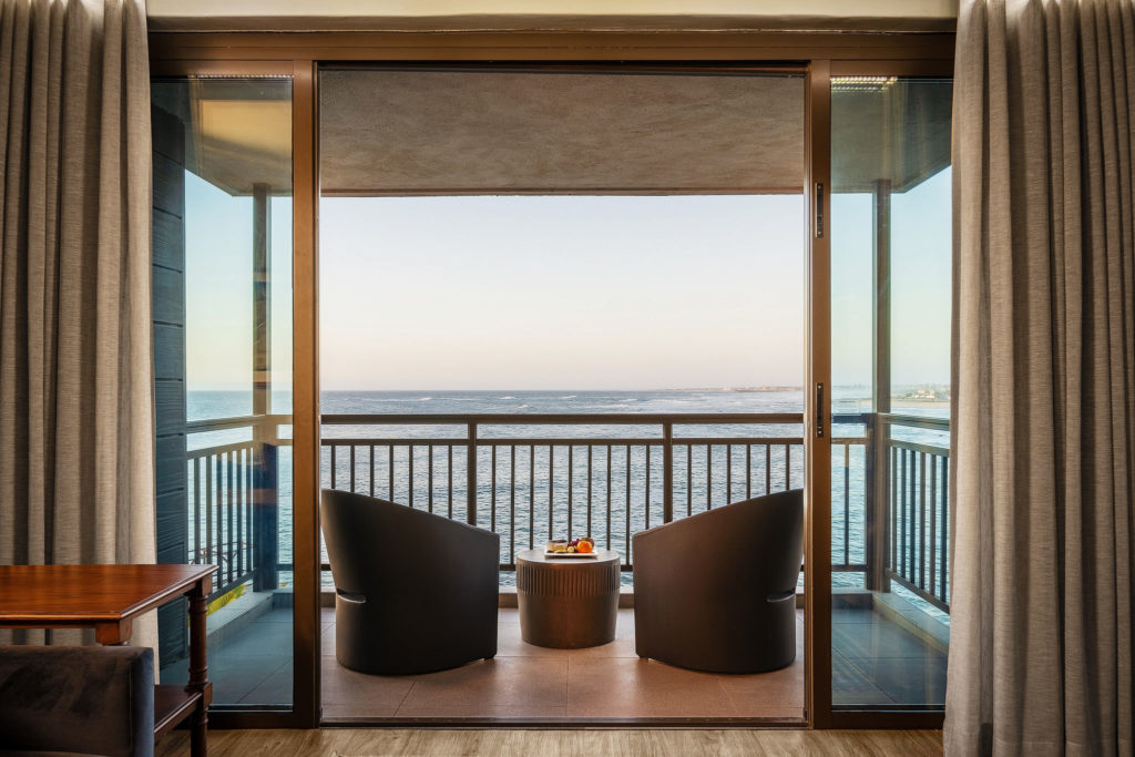 Sea-facing balcony of a Luxury Suite at Strand Hotel Swakopmund with lounge chairs, an ocean-view table setting and Atlantic waves rolling in