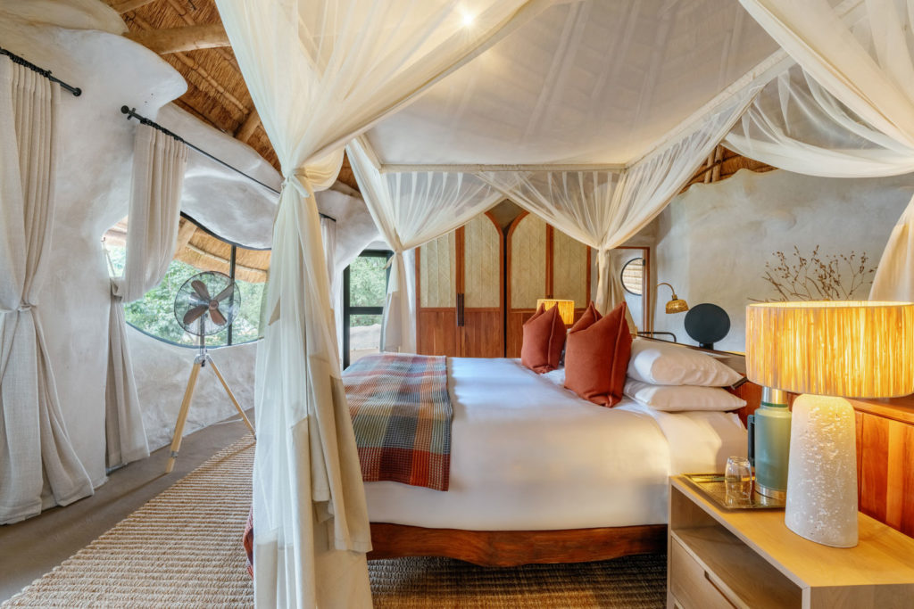 A canopied bedroom with a four-poster mosquito net, warm textiles and organic, curved plaster walls.