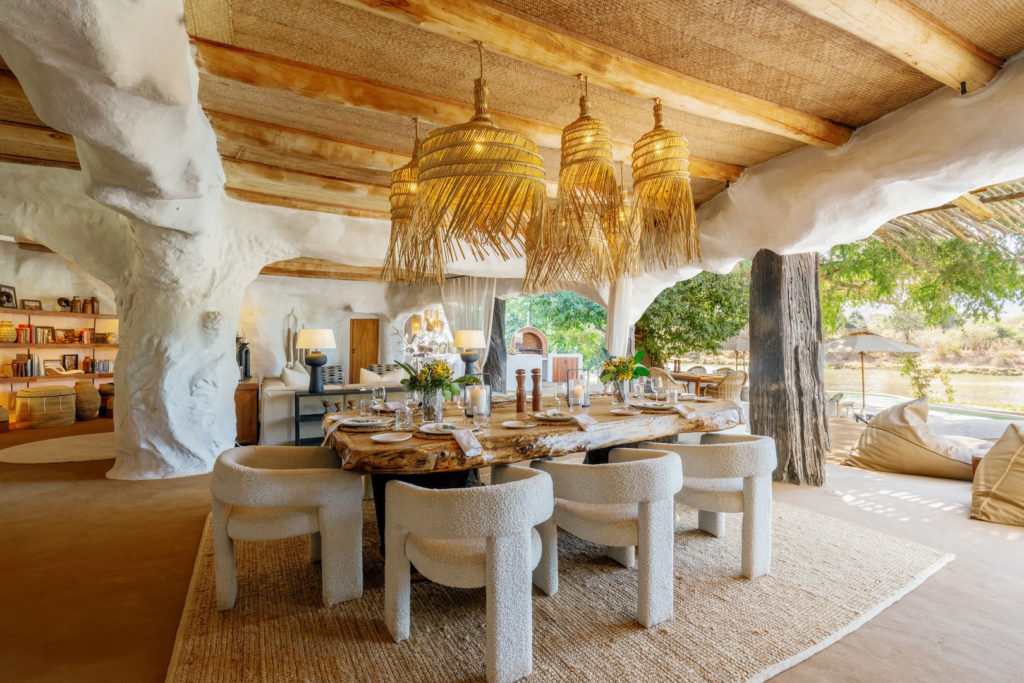 A sculptural dining area with a live-edge wooden table, woven pendant lights and river views beyond.