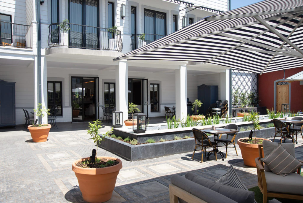 Courtyard dining area at The Weinberg Windhoek with striped awning, water feature and al fresco seating around the heritage building