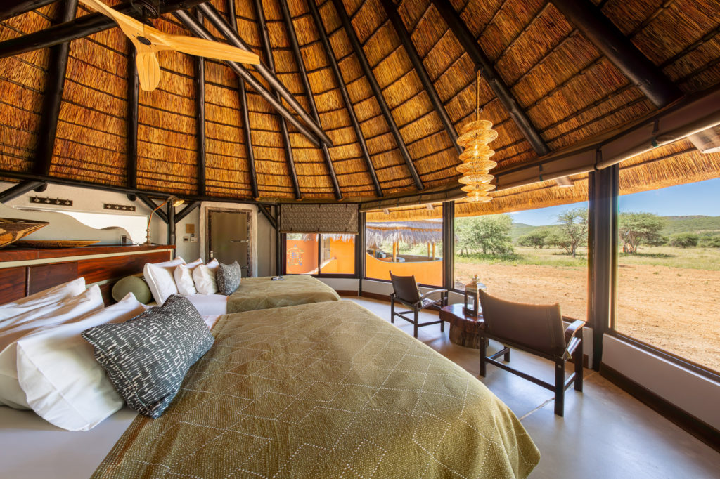 Twin-bed chalet interior at Okonjima Luxury Bush Camp with thatched ceiling and reserve views