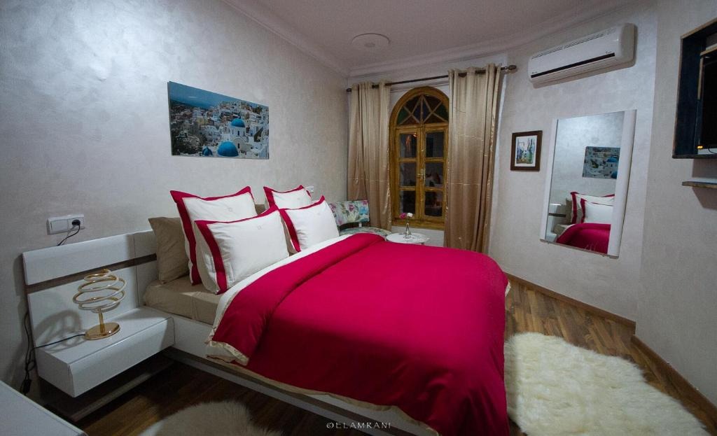 Bedroom at Hôtel Ziryab with a crimson bedspread, arched wooden window and Santorini-themed artwork above the headboard