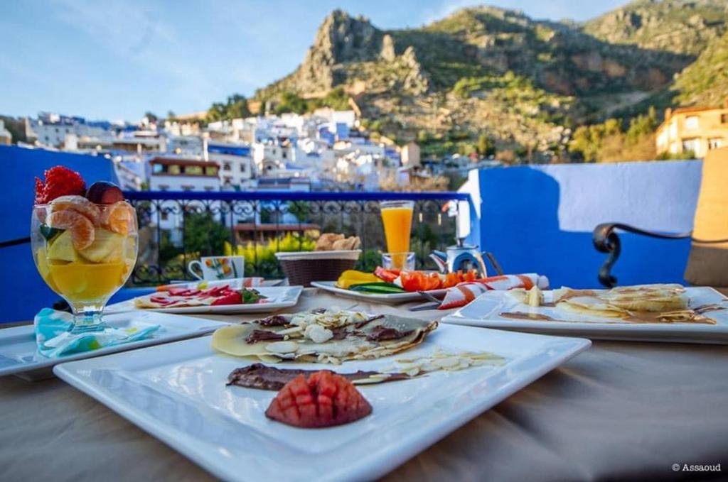 Breakfast spread of crepes, fresh fruit and juice on a terrace overlooking Chefchaouen's blue rooftops and the Rif Mountains