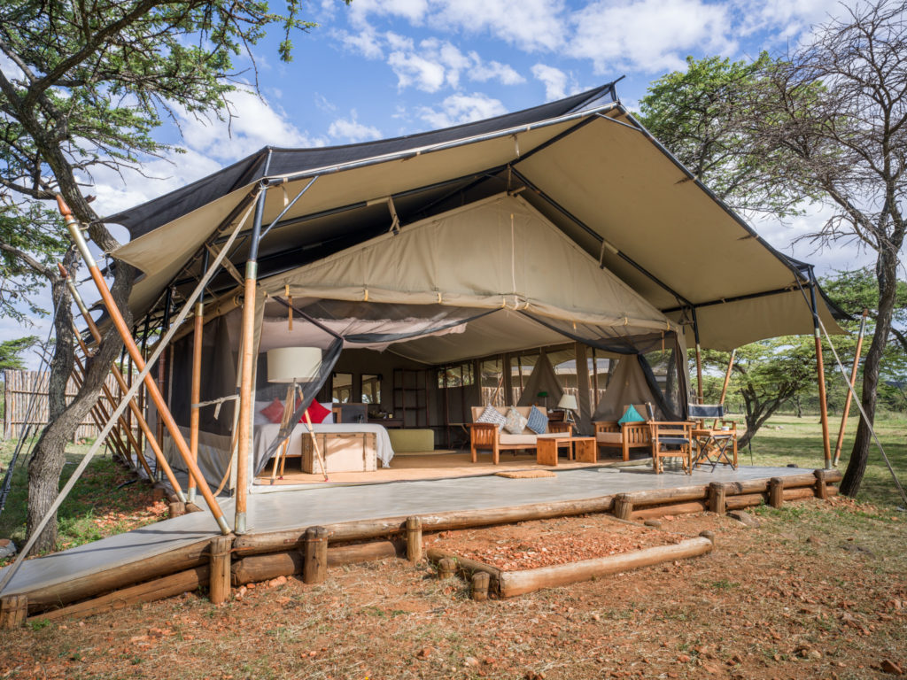 Superior double tent at Kandili Camp with a ramp up to the deck, its open canvas front showing the bed, sofa, armchairs and director's chairs.