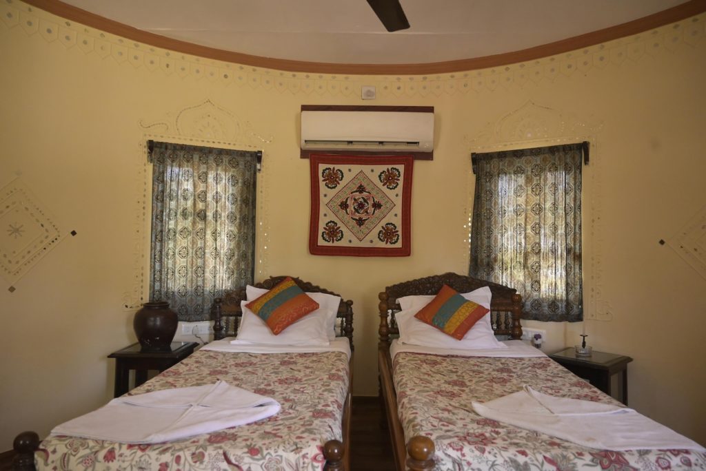 Twin beds beneath a Kutchi mirror-work wall hanging and lippan wall detail