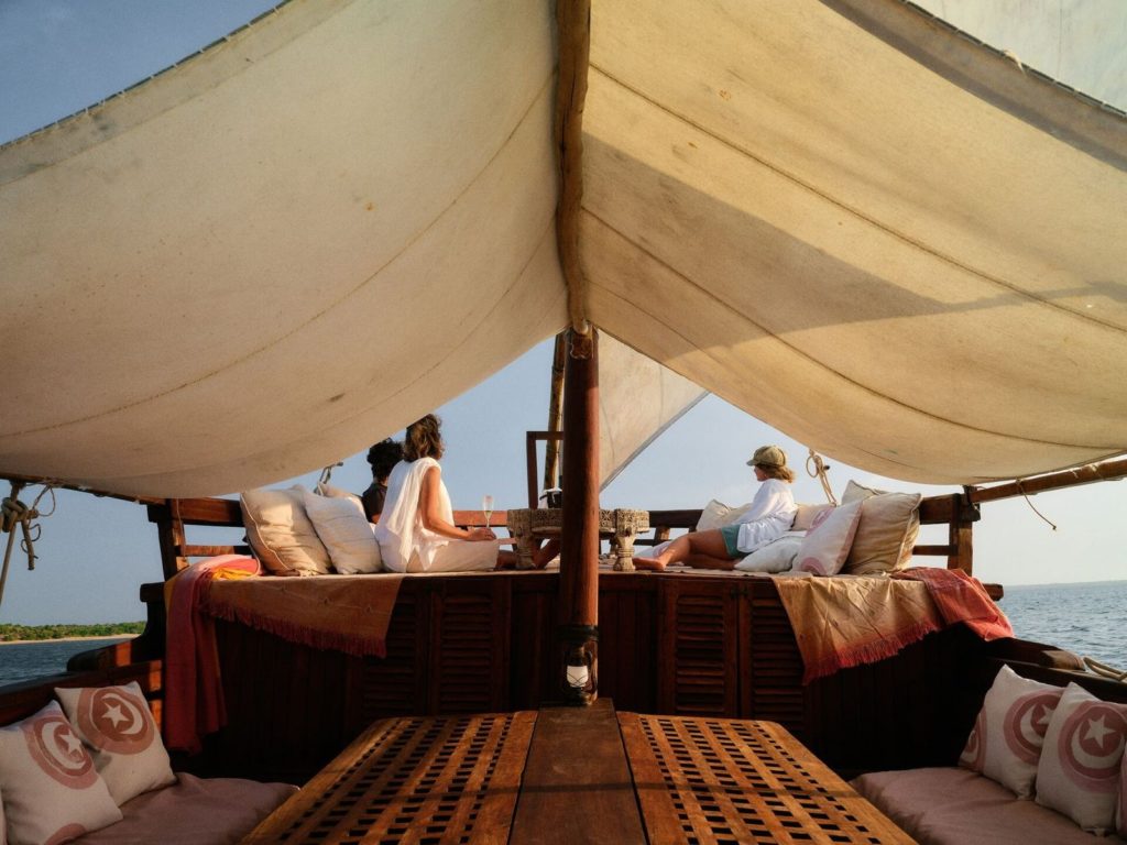 Guests lounge on cushioned decks under canvas shade during a sundowner dhow cruise off Lamu in golden evening light.