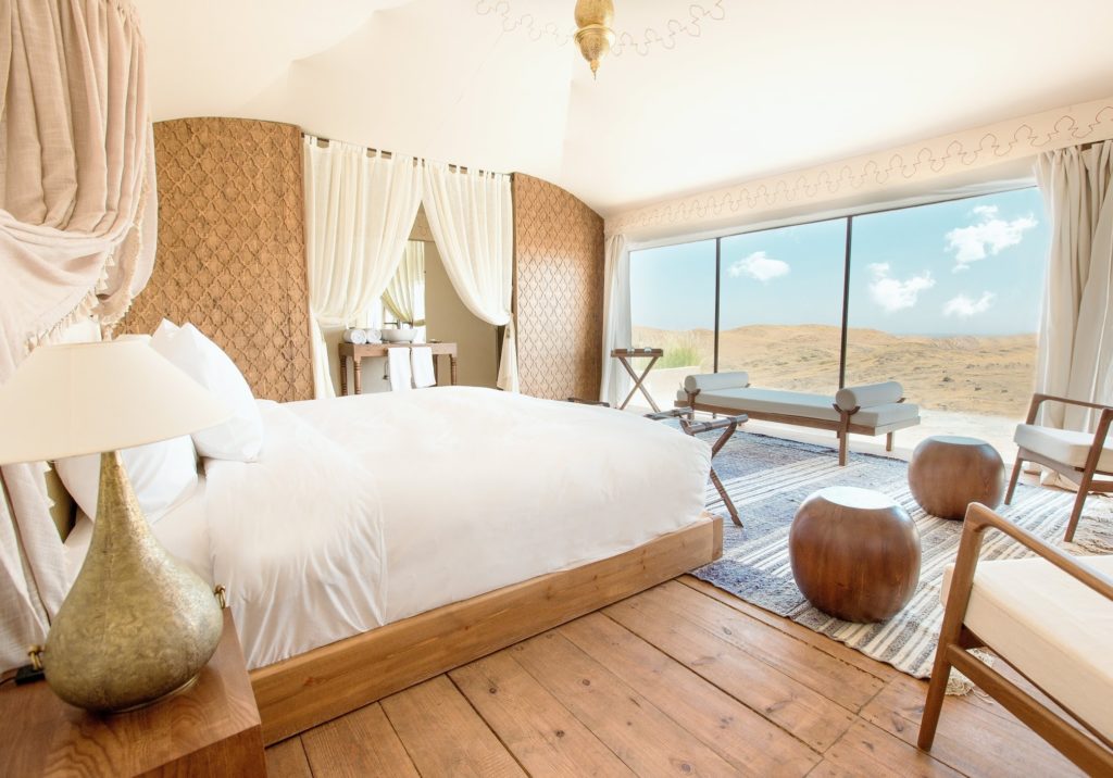A tented bedroom at The White Camel with wooden flooring and full-height glass looking out over the desert.