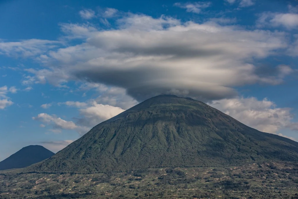 Lenticular cloud crowning the forested cone of a Virunga volcano, with a second peak rising in the distance