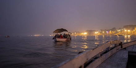 Boat ride on the Ganges at night, with passengers sheltered under a canopy and city lights shimmering on the water.