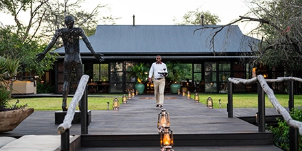 The central lodge at Mukwa River Lodge is approached along a wooden deck lined with lanterns, creating a warm and welcoming evening atmosphere.