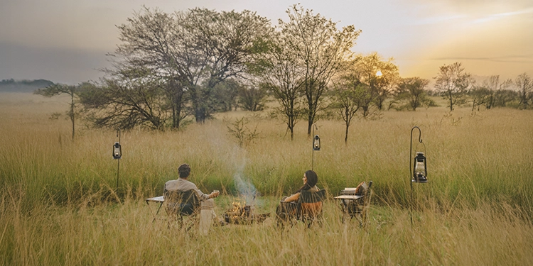 Guests enjoy a classic Serengeti sundowner beside a campfire, surrounded by tall grasses and soft golden evening light in the Lamai Wedge.
