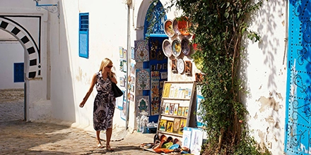 Woman browsing colourful artisan ceramics and paintings along a narrow cobbled street in Sidi Bou Said, Tunisia.