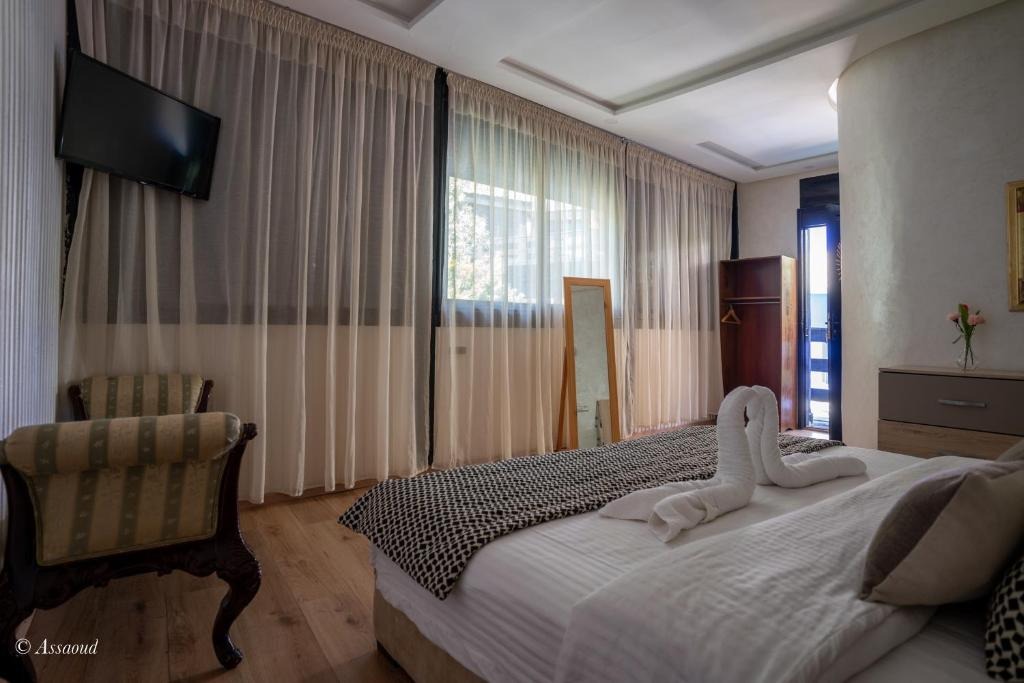 Guest room with sheer curtains, wall-mounted television and towels folded into a swan on the bed