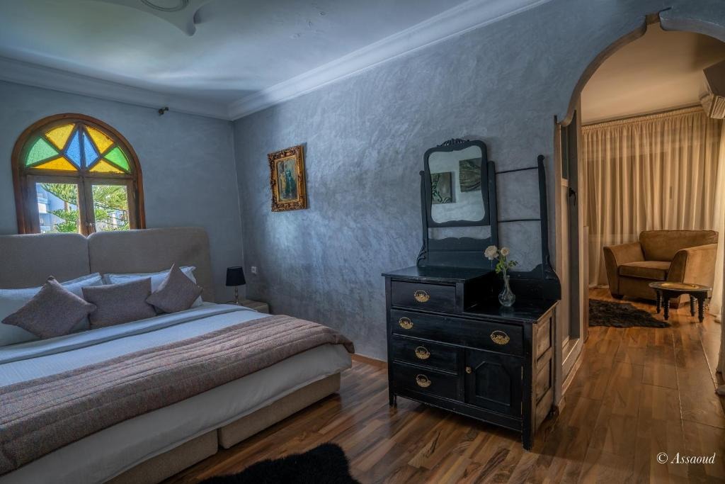 Bedroom with a stained-glass window, antique dresser and mirror leading through to a seating area