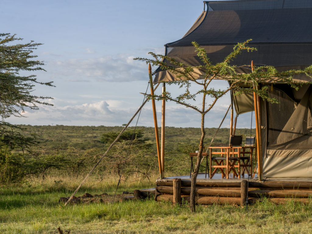Superior tent veranda with two director's chairs looking out over acacia scrub and open plains in late afternoon light, Maasai Mara, Kenya.