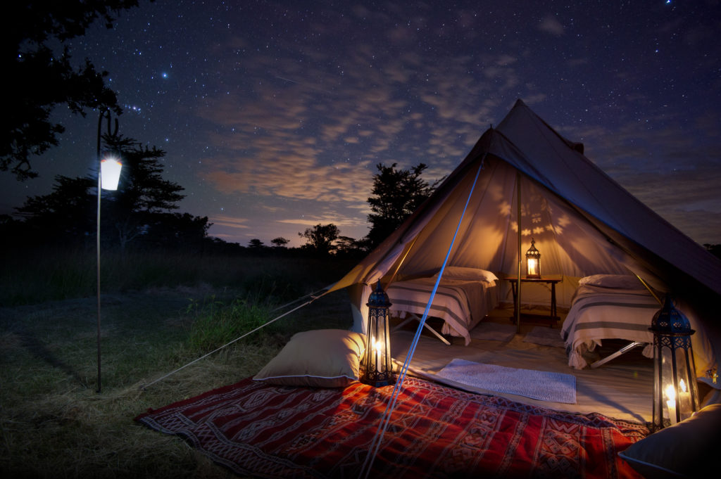 Candlelit bell tent with twin beds, Moroccan lanterns and a red kilim rug beneath a starry sky on an El Karama fly camp.