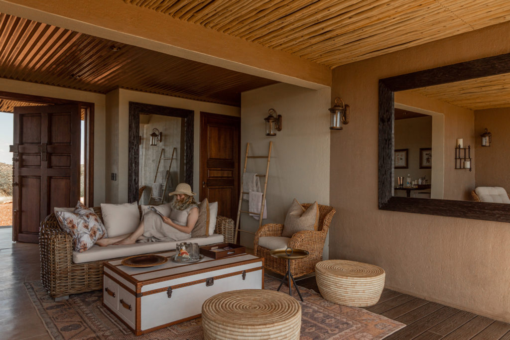 A guest relaxes on a wicker sofa within a private suite lounge, furnished with woven ottomans and antique mirrors