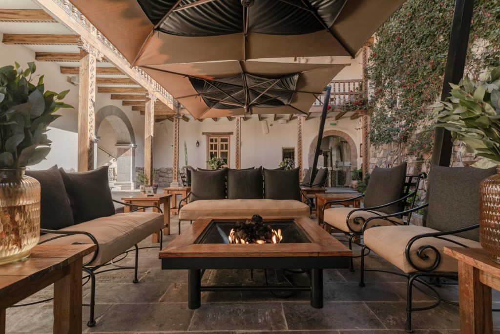 Cantilevered umbrellas shade a lounge seating area in the courtyard, framed by carved wooden columns and a flowering bougainvillea wall.