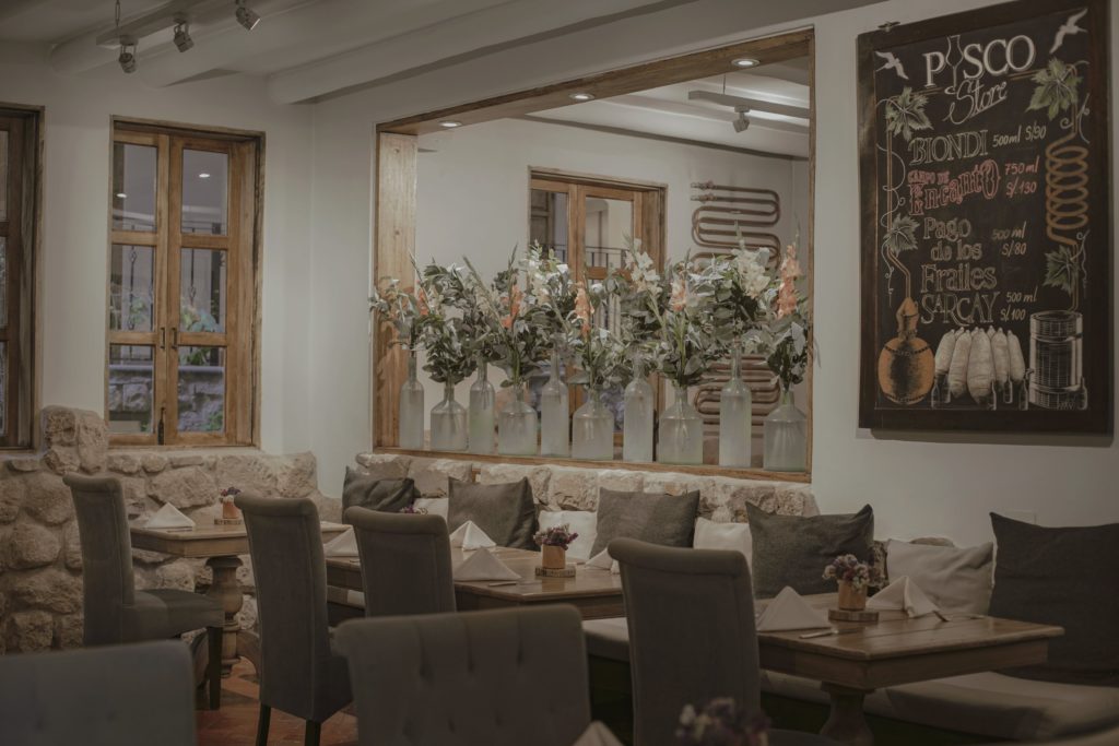 A dining nook at Piedra & Sal with stone half-walls, upholstered banquette seating, and a mirrored display of floral-filled glass bottles.