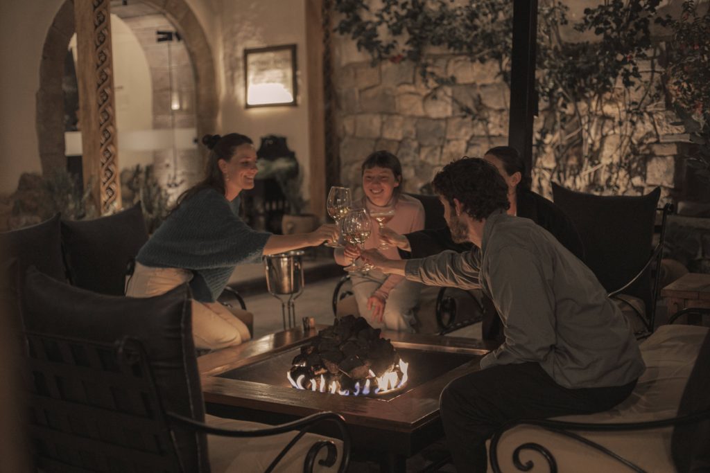 Guests raise wine glasses beside a glowing fire pit table in the candlelit courtyard at Piedra & Sal.