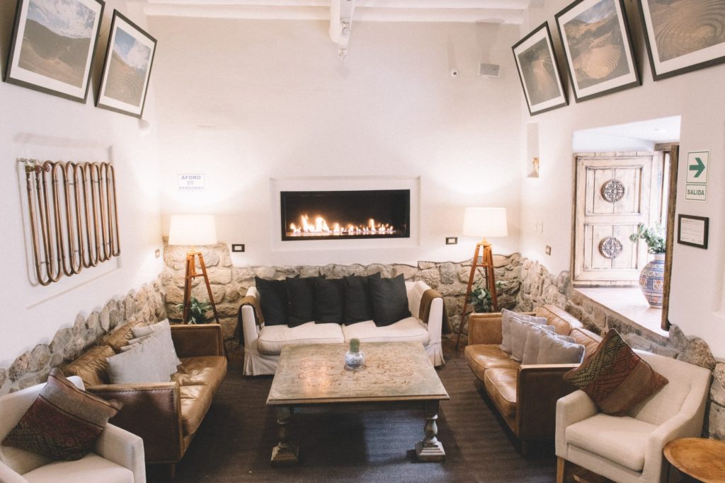 A stone-walled lounge with leather sofas, a lit gas fireplace, and framed aerial photographs of Peruvian landscapes.