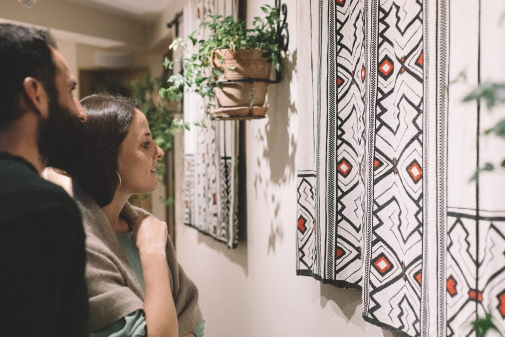 Guests admire hand-woven Amazonian textiles displayed on a wall alongside potted greenery in the Xapiri Ground art gallery.