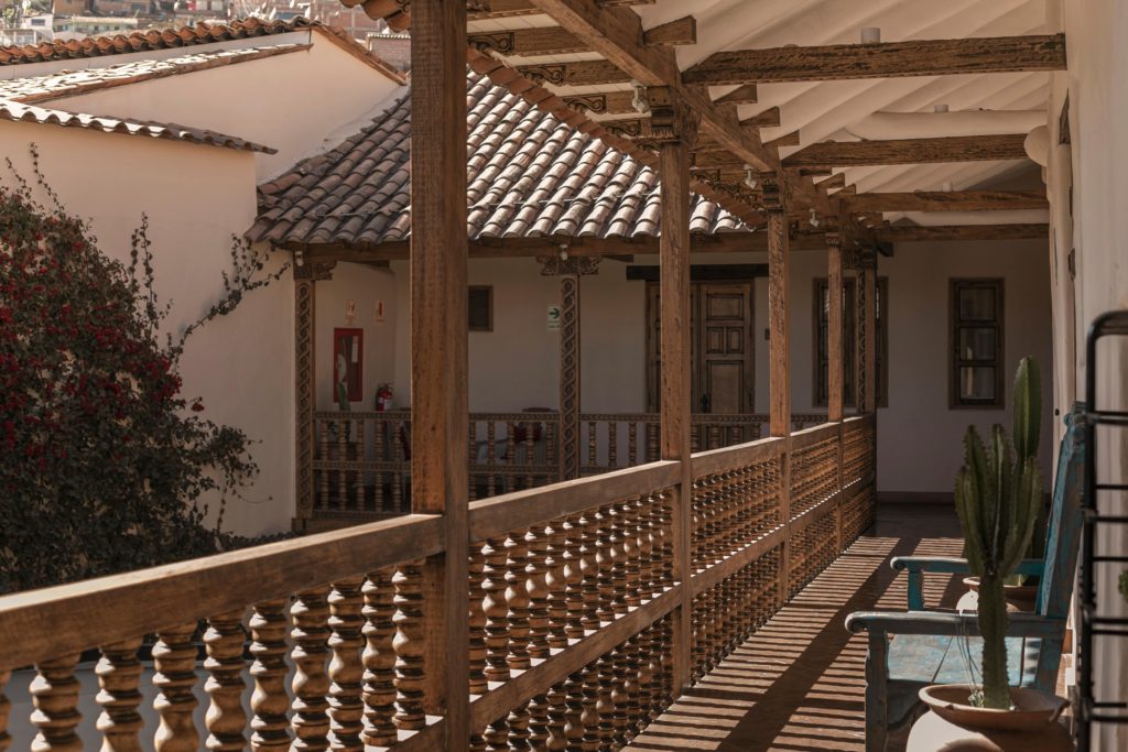 A wrap-around wooden balcony with carved balustrades overlooking Cusco's terracotta-tiled rooftops and a flowering bougainvillea.