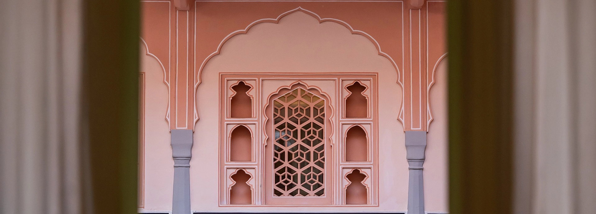 A symmetrical view of an intricately carved pink window frame set within traditional Rajasthani architecture.