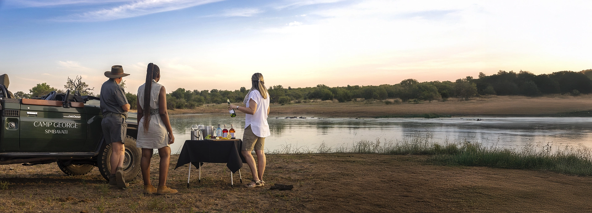 Guests enjoy sunset drinks beside a river after a game drive at Simbavati Camp George in the Timbavati Private Nature Reserve.