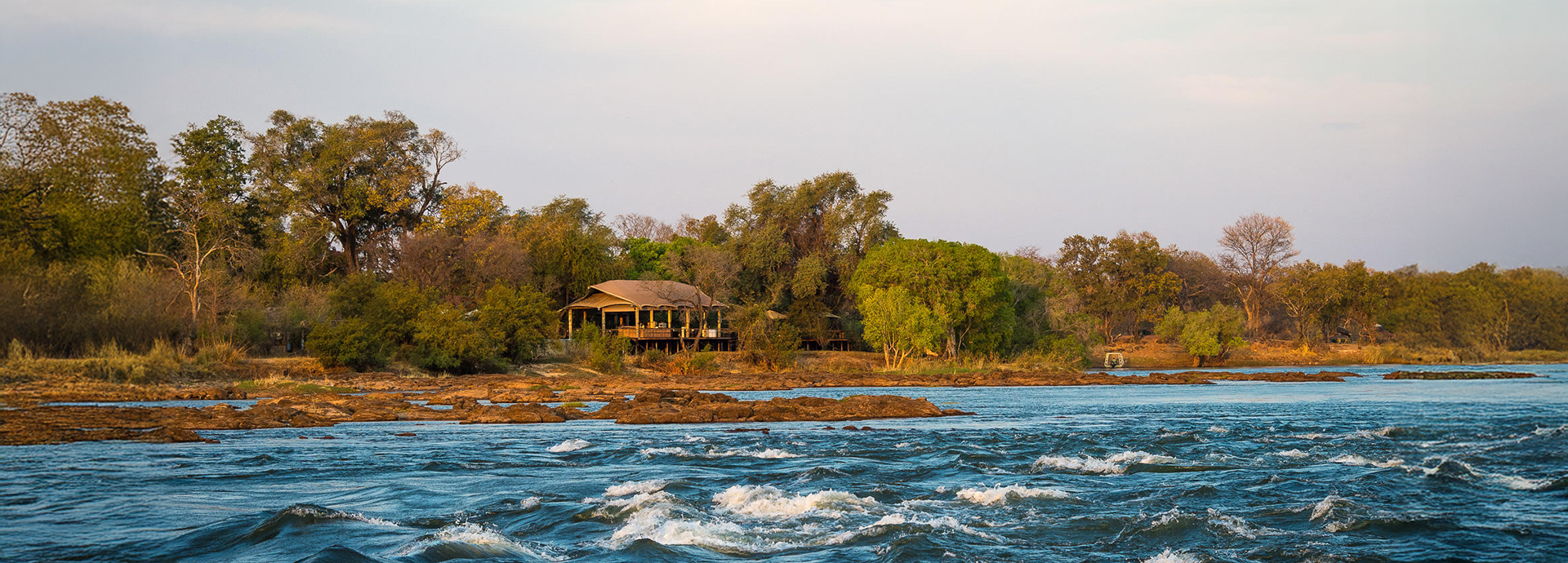 Scenic riverbank view of Toka Leya Camp framed by forest and rapids