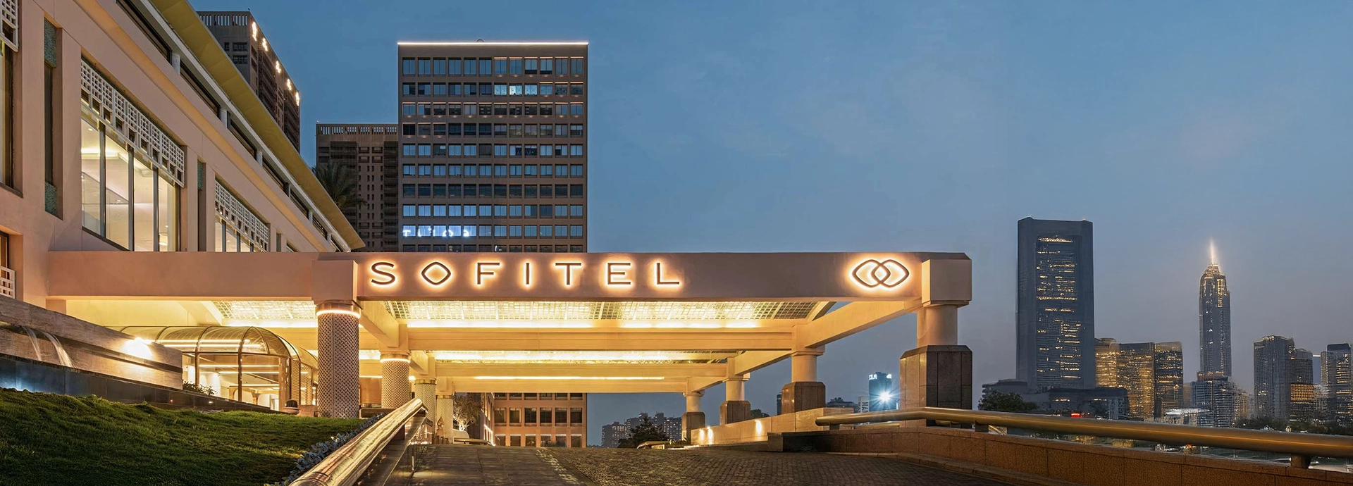 The Sofitel Cairo Nile Hotel entrance glows warmly at dusk, framed by the city skyline and the soft blue evening light.