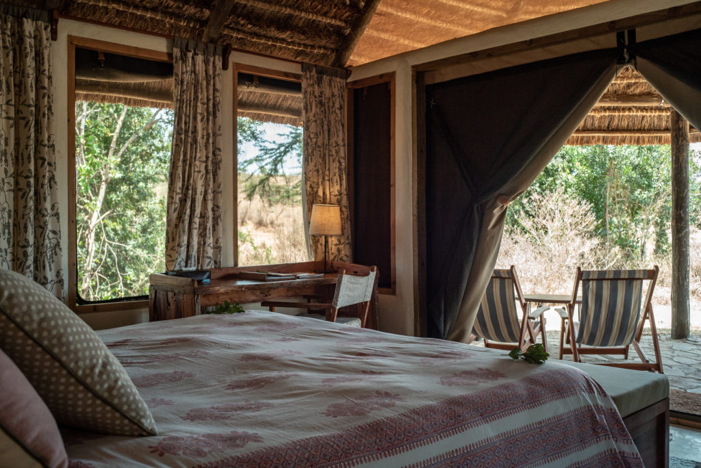 Double bed in a thatched El Karama cottage, with a timber writing desk and doors opening onto a veranda with striped deckchairs.