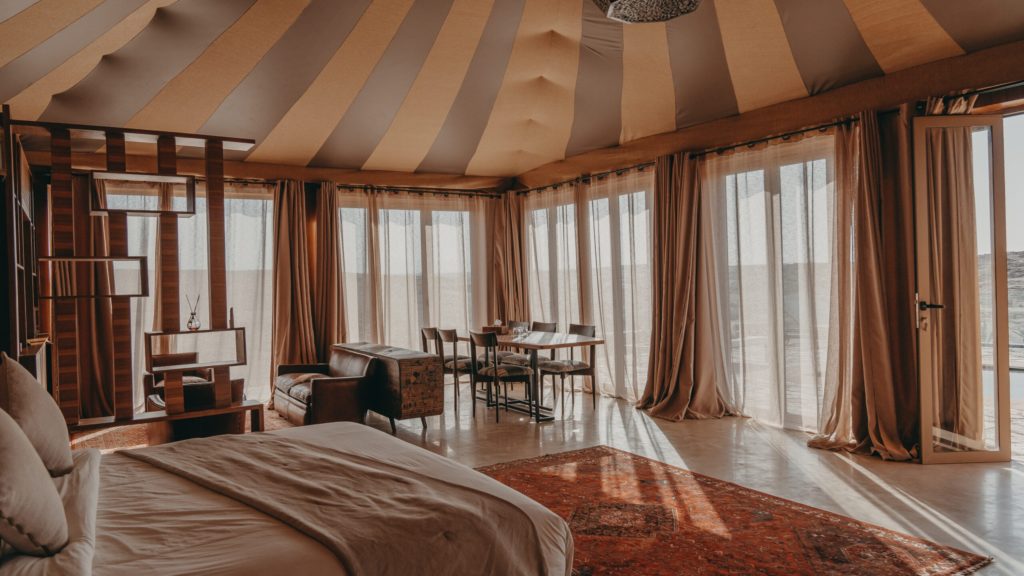A striped canvas suite with a leather armchair, dining table and floor-to-ceiling curtains framing the dunes.