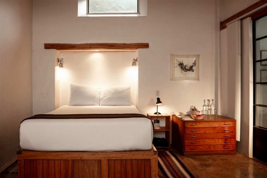 Sunken headboard nook with soft lamplight above a queen bed and antique wooden dresser at El Albergue Ollantaytambo