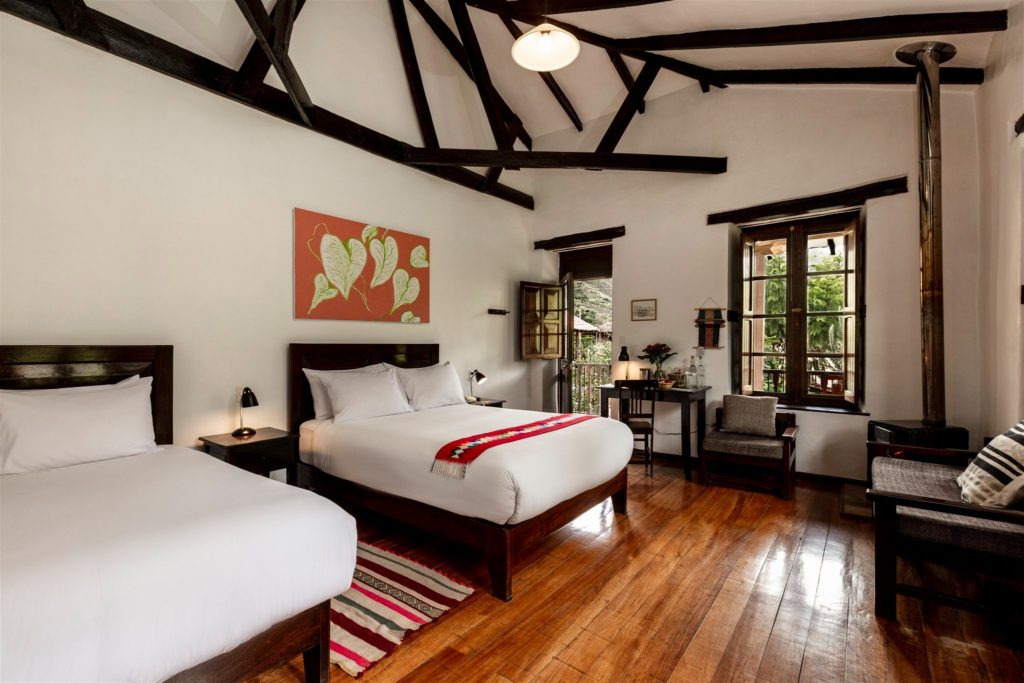 High-beamed bedroom with two beds, colourful Andean rug and a private balcony opening onto garden views