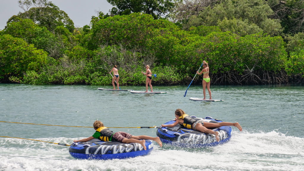 Children on towed inflatable tubes skim across the water as three guests paddleboard past mangroves near Manda Bay Lodge.