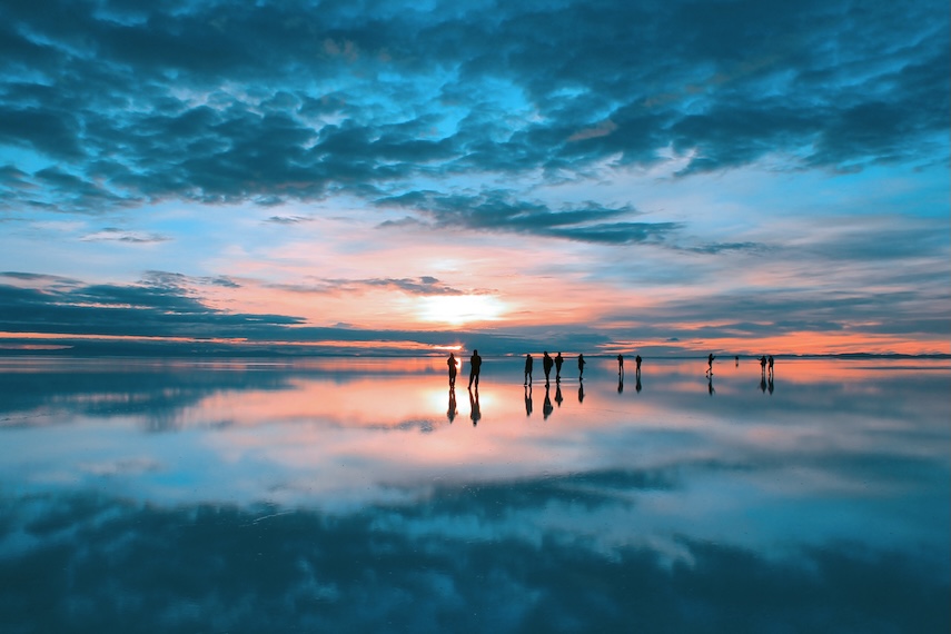 Sunrise at Salar de Uyuni, Bolivia, with a group of travellers walking across the mirrorlike surface 