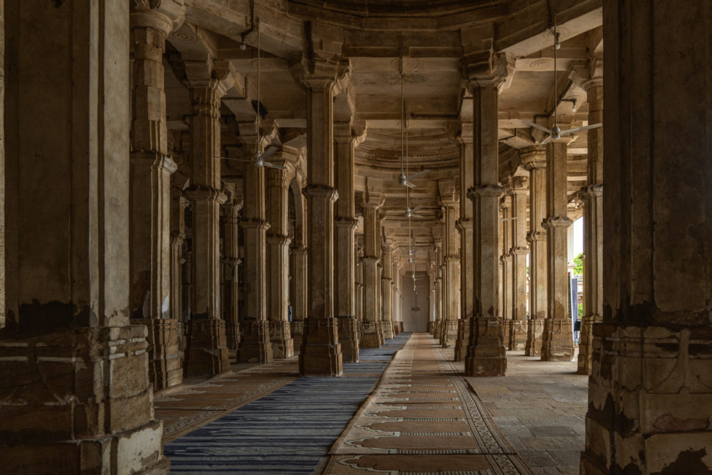 Rows of carved stone columns inside a covered mosque corridor in Ahmedabad
